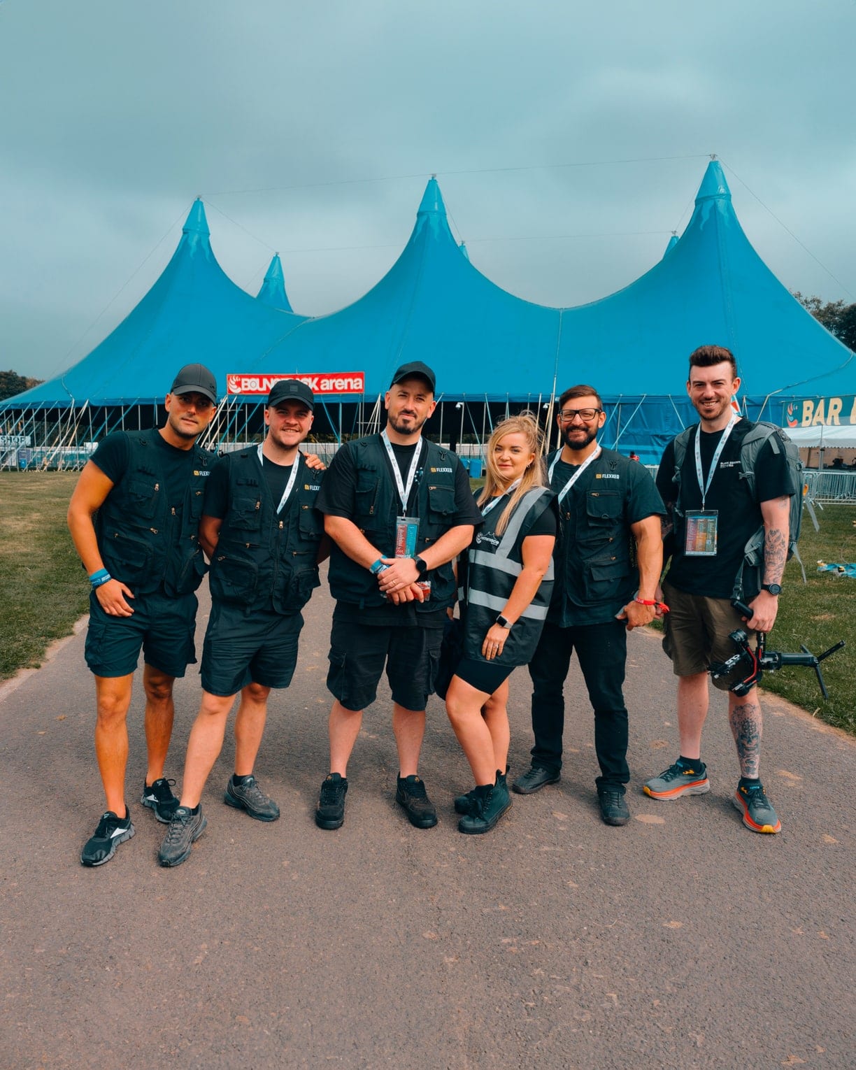 Crew on site at a festival, gathered in front of the blue marquees