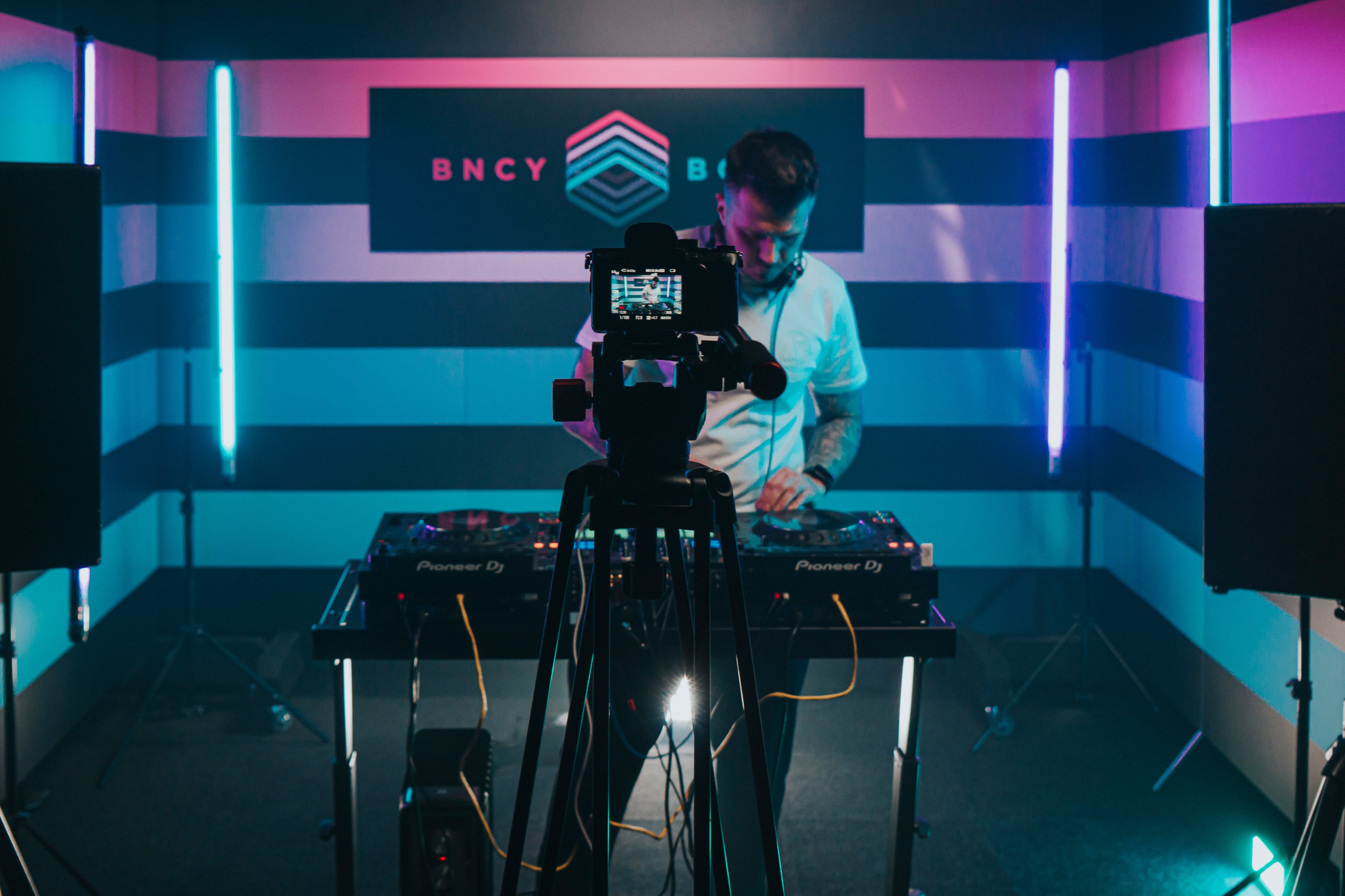Camera operator filming a DJ on a set lit by pink and teal LED strips