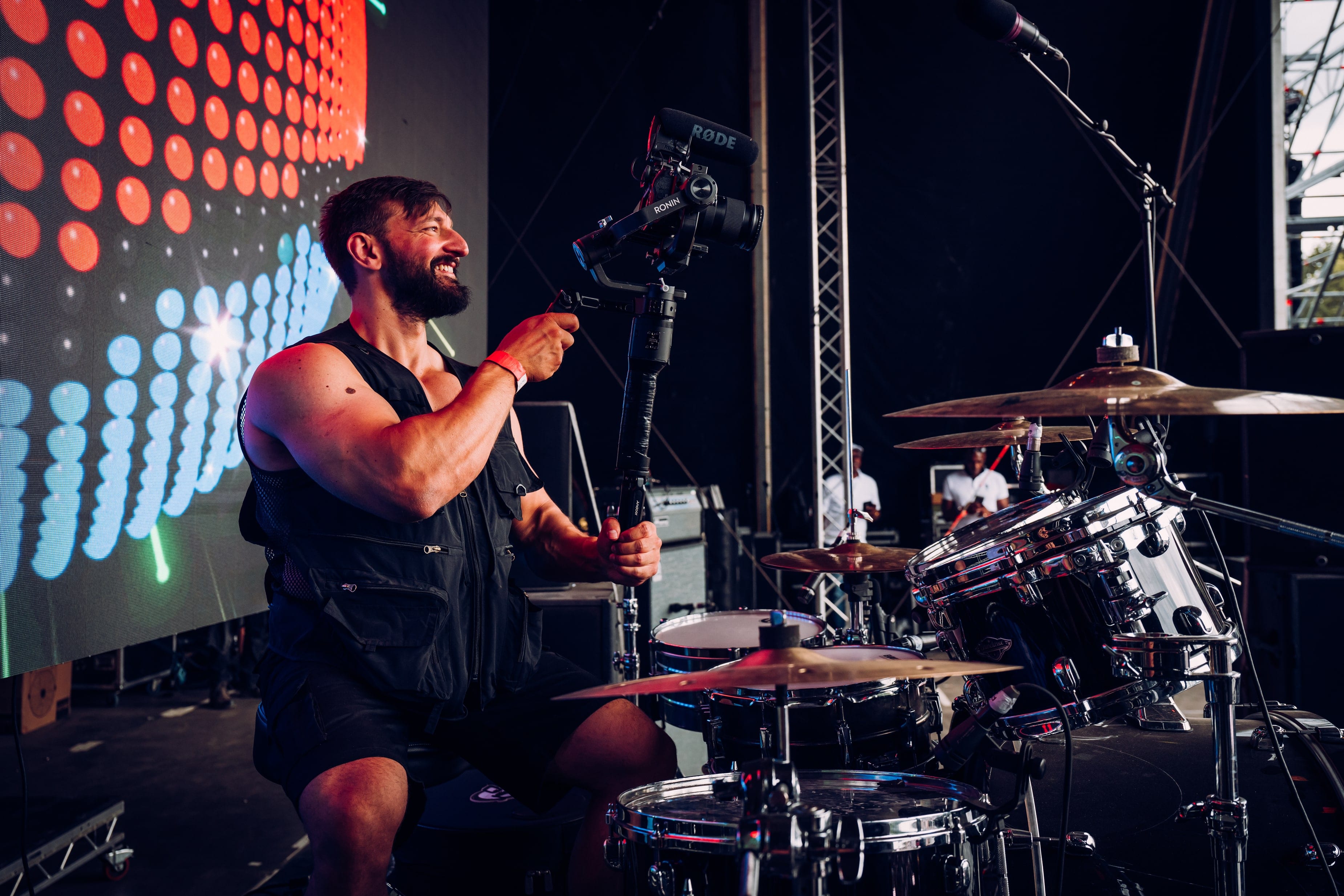 Camera operator on stage beside a drum kit, LED wall lit behind
