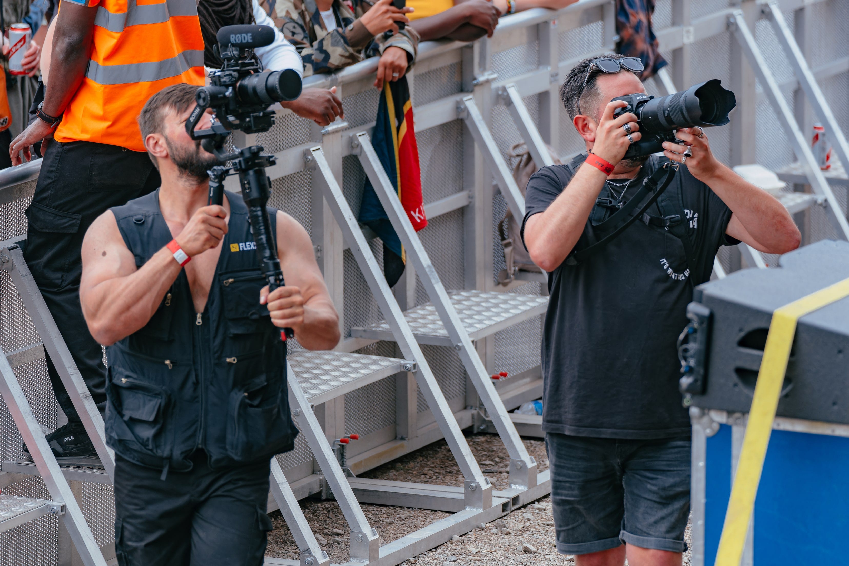 Two camera operators filming from the pit at a festival barrier