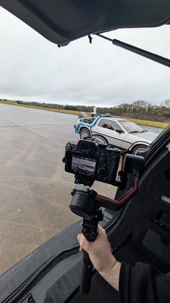 A DeLorean parked on an airfield runway, framed on a camera monitor