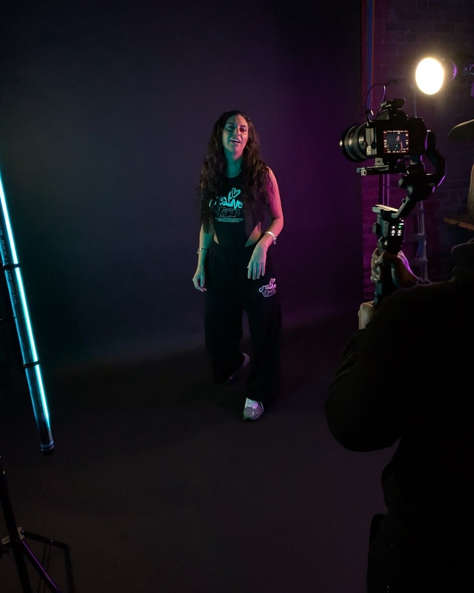 A portrait session in progress in the studio, the subject lit against the backdrop and a camera framing her from the foreground