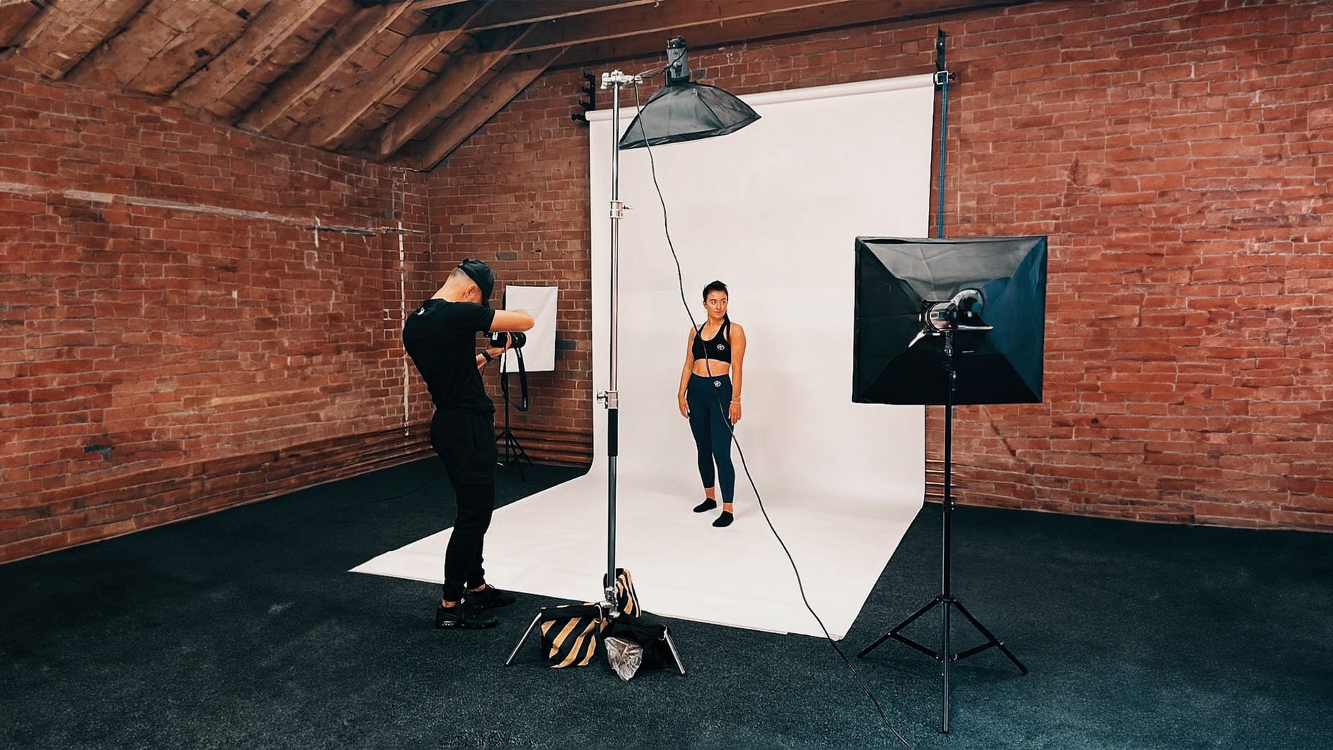 Portrait session in progress: photographer, model on a white backdrop and two softboxes against the brick wall