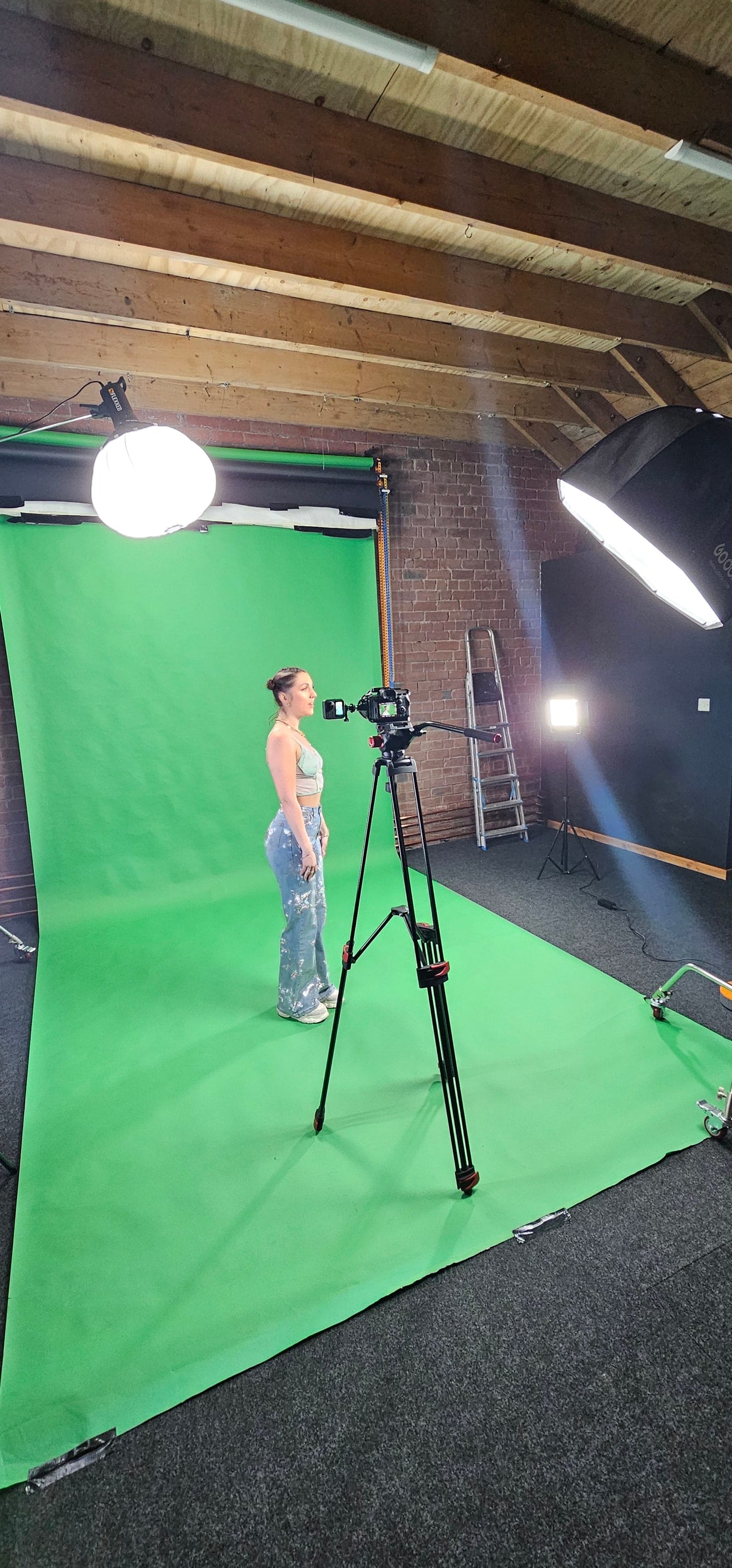 Wide view of the green screen with a subject standing and a camera on a tripod