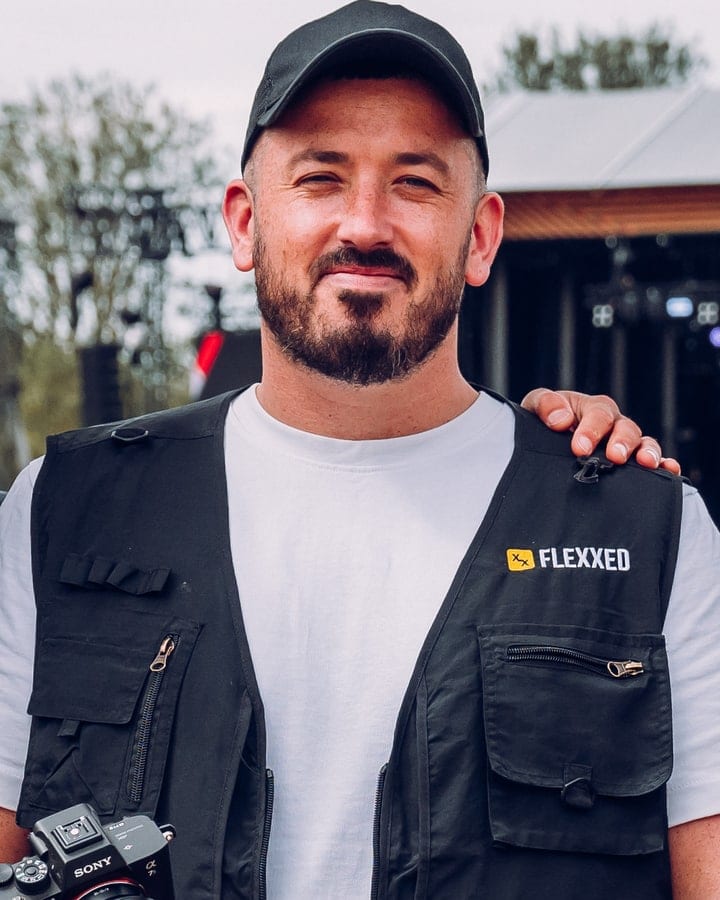 Mikey at Reggae Land in a Flexxed vest over a white tee, the crew arch behind him