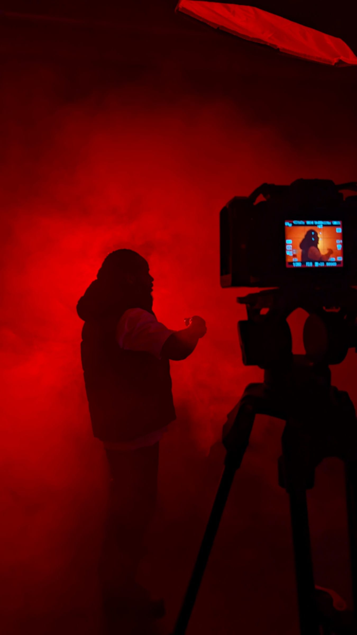A figure silhouetted against deep red studio light beside a monitor