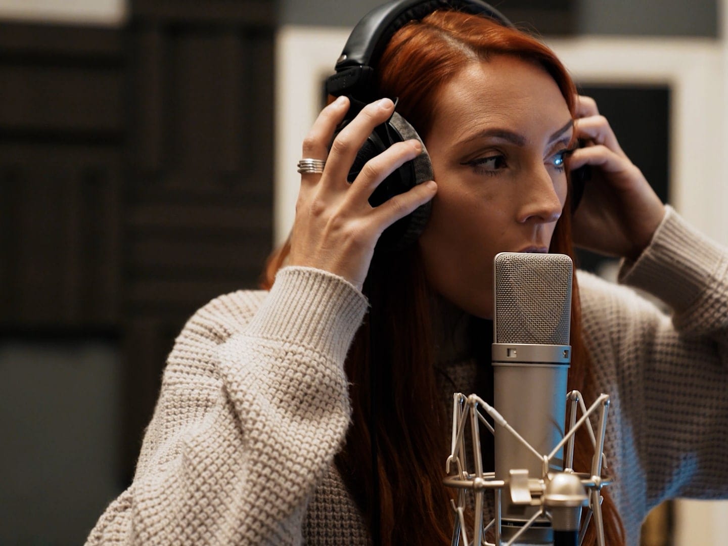 A singer in headphones at a condenser microphone in a recording booth
