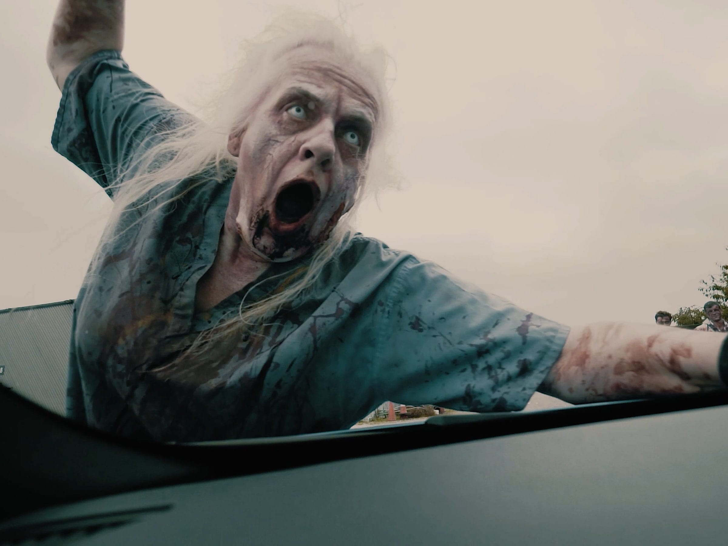 A zombie in torn clothes lunging across the bonnet of a car, shot for a horror film
