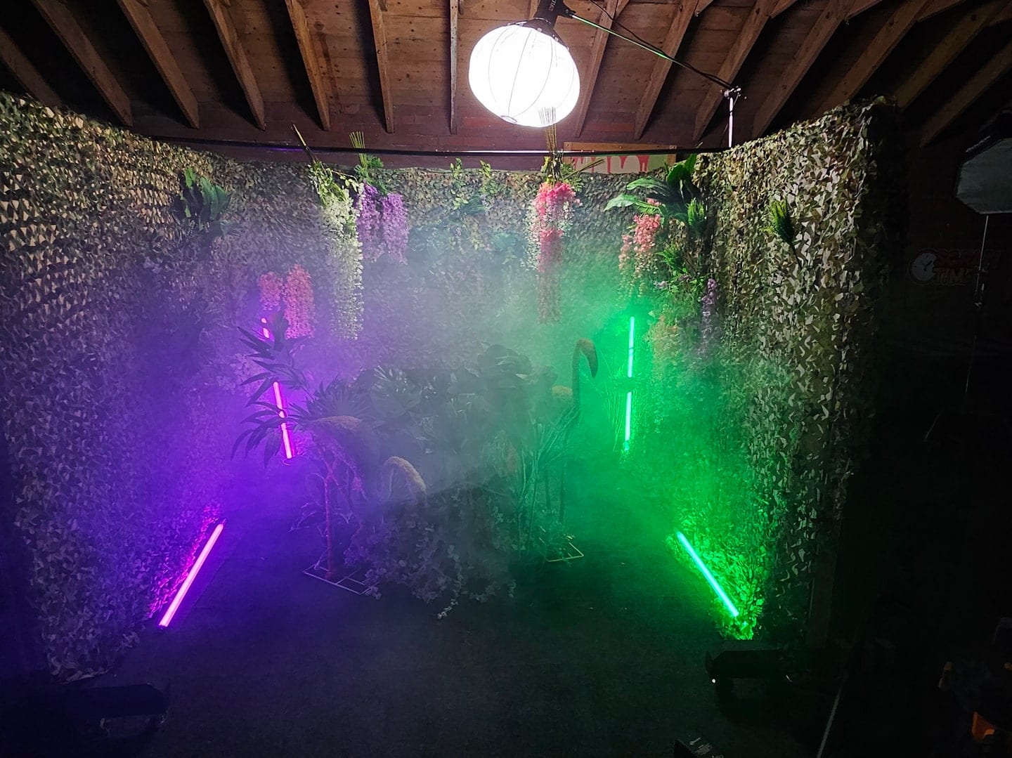 Green and magenta laser beams cutting through haze against a foliage backdrop