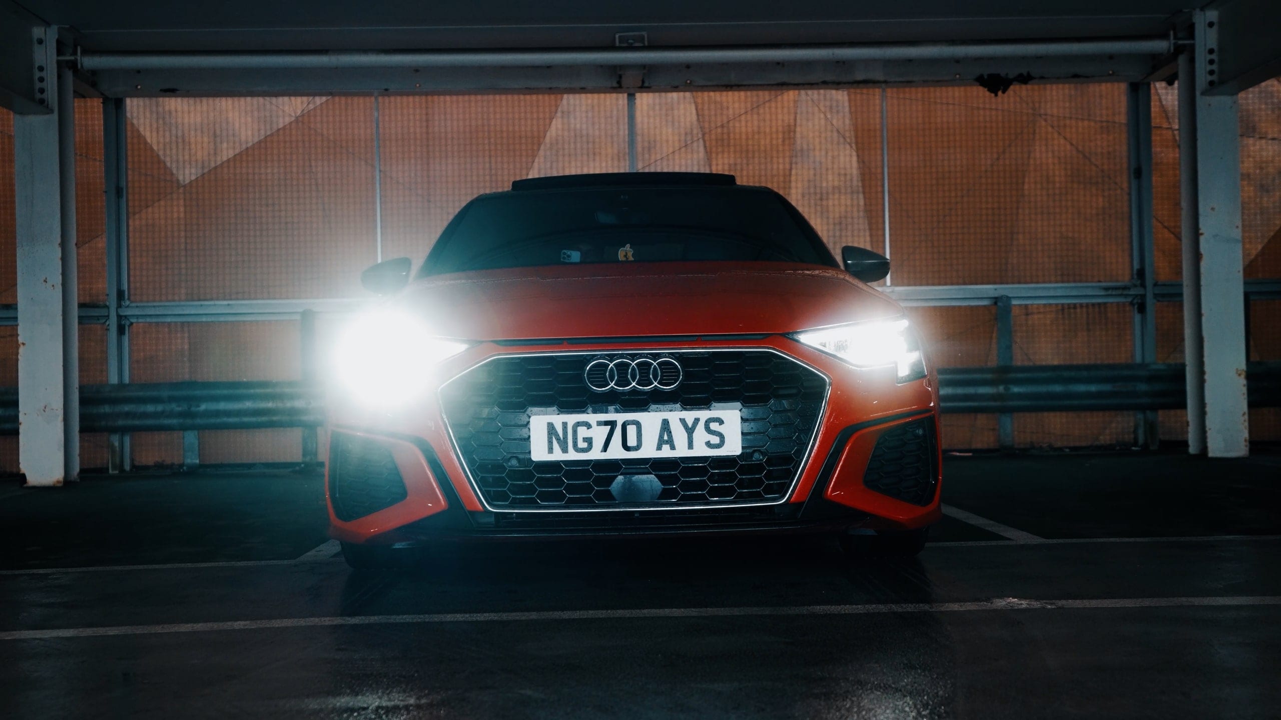 An Audi head-on in a dark space, headlights flared toward the lens