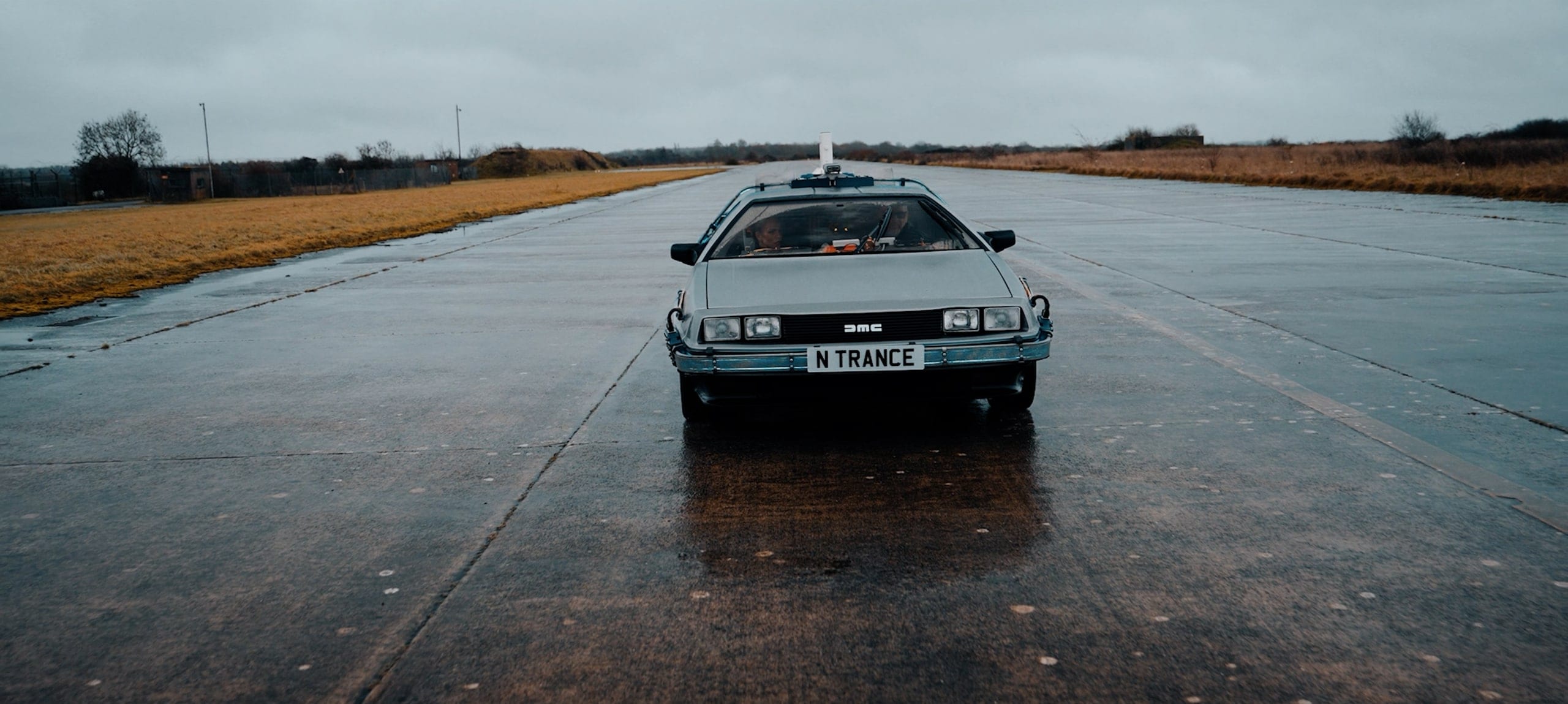 A DeLorean on a wet open road under a flat grey sky
