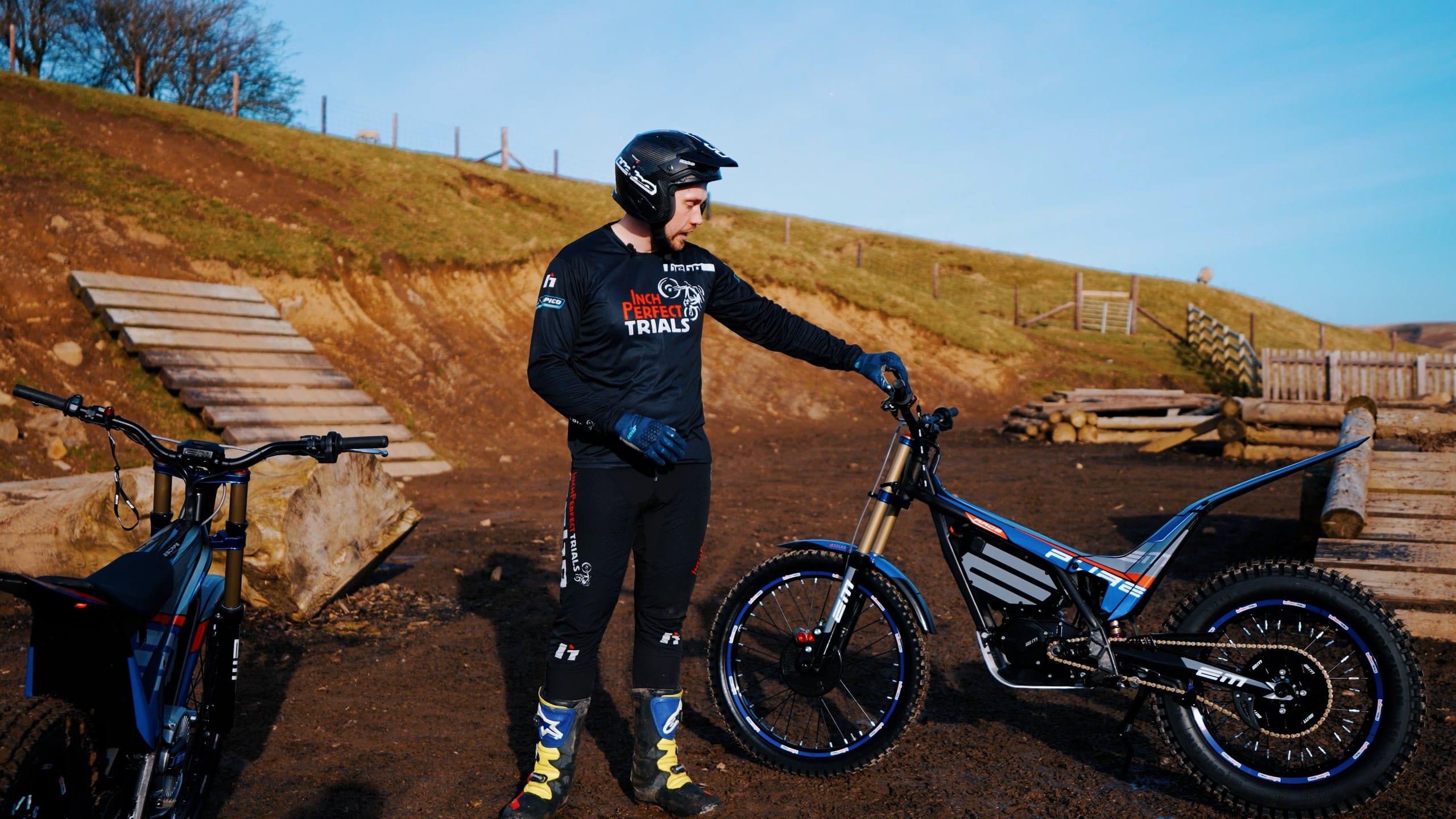A trials rider standing over an electric bike on a hillside course