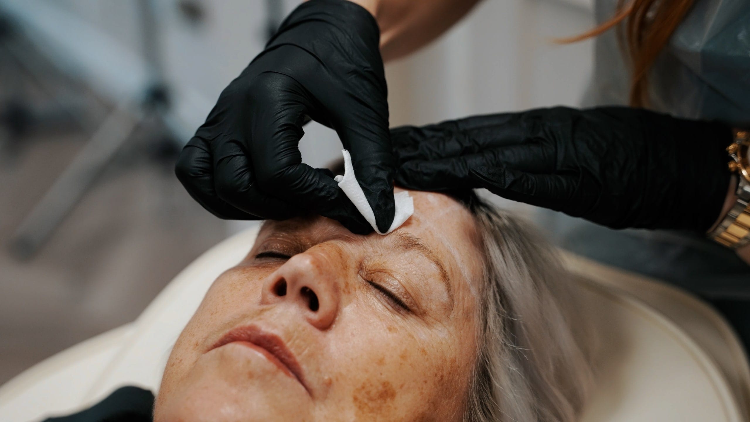 A gloved practitioner working on a client’s brow in an aesthetics clinic