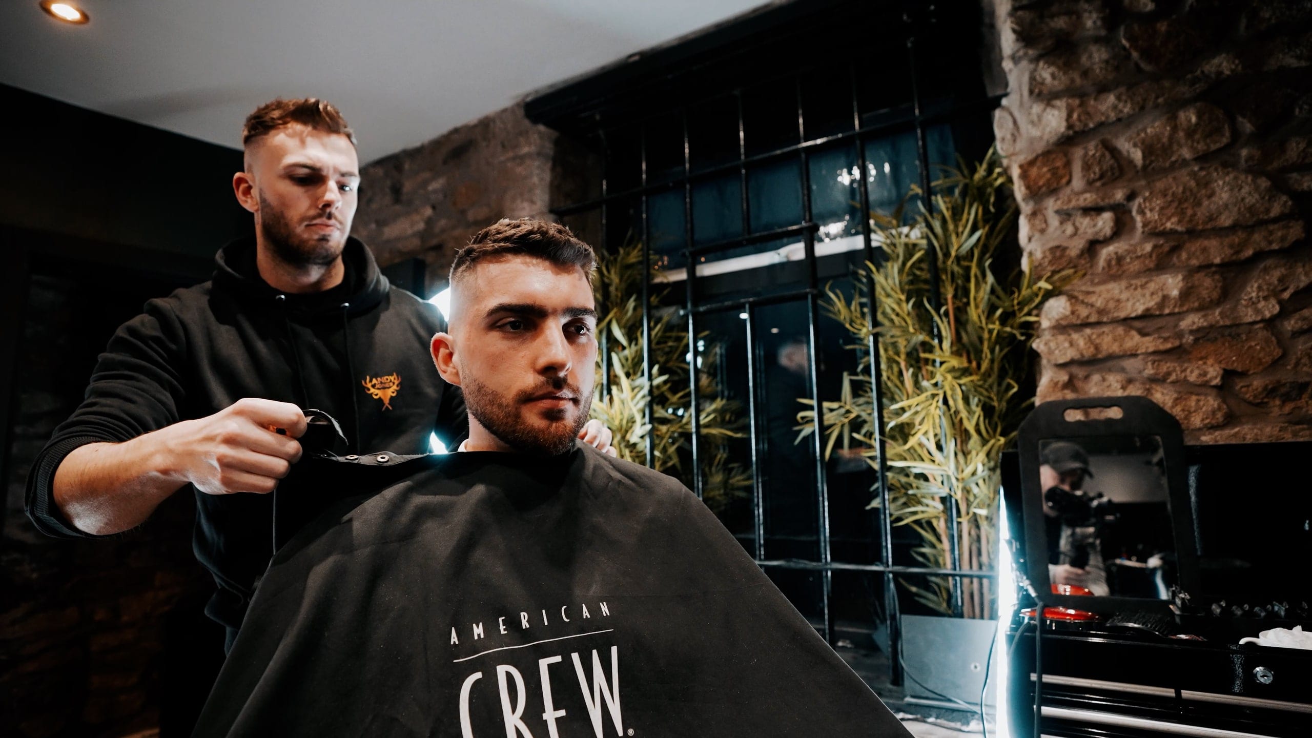 A barber cutting in a fitted shop, the client caped and lit from the window