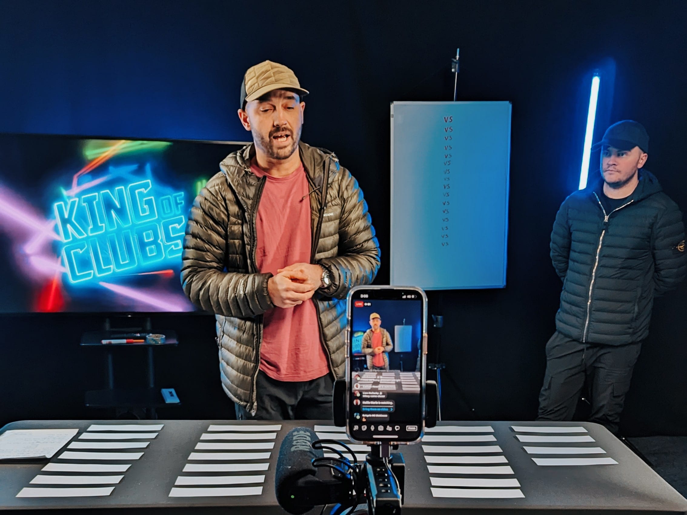 Presenter at a lit desk with a monitor and a camera in front
